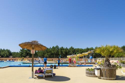 une piscine dans un complexe hôtelier avec des gens assis sur des chaises et un parasol dans l'établissement camping les oyats, à Seignosse