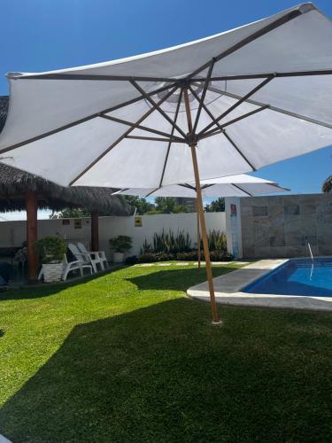 ein großer weißer Regenschirm neben einem Pool in der Unterkunft Departamento equipado muy cerca de Playa in Manzanillo