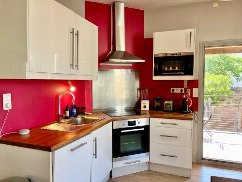 a kitchen with white cabinets and a red wall at La circulade - Maison de caractère avec jardin in Bram