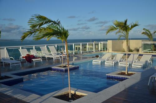 a swimming pool with white chairs and palm trees on a building at Apartamento JTR Maceió in Maceió