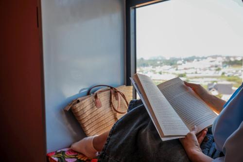 a person reading a book in front of a window at Âm Ấm Đà Lạt Boutique Hotel & Cozy Bistro in Khu Chi Lăng