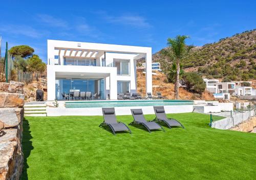 a house with a lawn with chairs in front of it at Villa BuenaVista Hills - Sea View - Infinity Pool - Parking - Grill in Málaga
