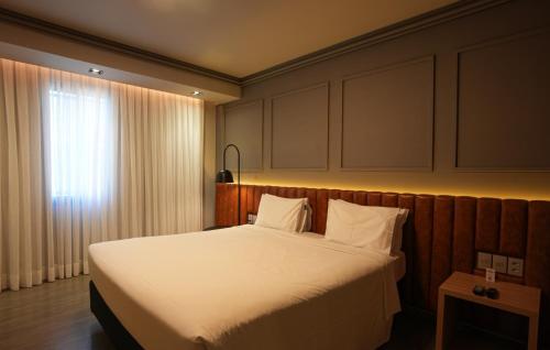 a bedroom with a bed with white sheets and a window at Grand Mercure Curitiba Rayon in Curitiba