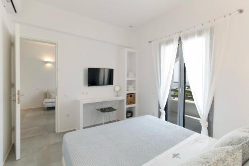 a white bedroom with a bed and a tv at Alexander Suites in Drios