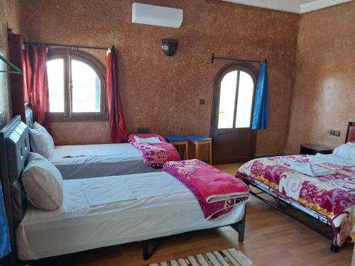 a bedroom with two beds and two windows at Sud Est Palace in Aït Ridi