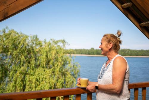 a woman standing on a porch with a cup of coffee at Agroturystyka nad jeziorem-Herrmann hof in Dejguny
