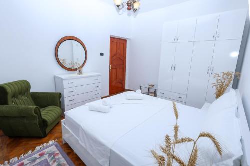 Un dormitorio con una cama blanca y una silla verde. en The Cozy 2 room apartment Berat, en Berat