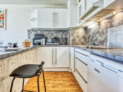une cuisine avec des placards blancs et une chaise noire dans l'établissement Apartment Les Alizés by Interhome, à Lacanau