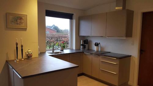 a kitchen with brown cabinets and a large window at Feriehus i Sæby nær by, skov og strand in Sæby