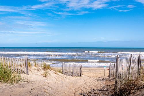 a sandy beach with a fence in front of the ocean at D4414 Exhibit Sea. Soundfront, Stunning Sunsets, Pier, Private Pool & Hot Tub! in Sanderling