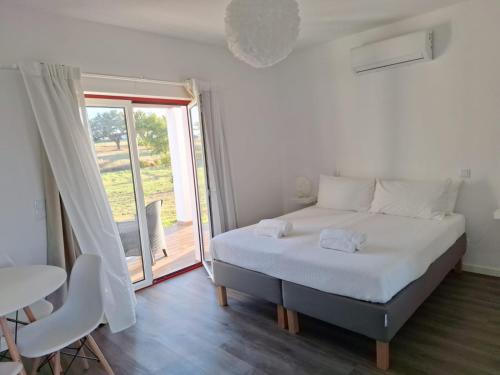 a white bedroom with a bed and a balcony at Monte da Isabel in Vale de Água