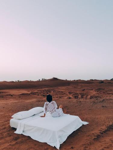 a woman sitting on a bed in the desert at Silent Camp in Mhamid