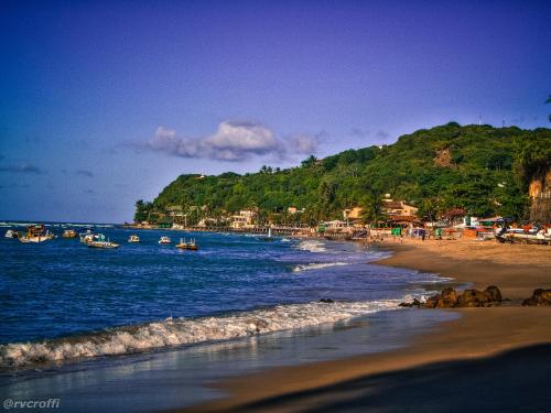 a beach with boats in the water and a mountain at Pousada da Pipa in Pipa
