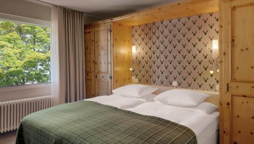 a bedroom with a bed with a green and white blanket at Morosani Posthotel in Davos