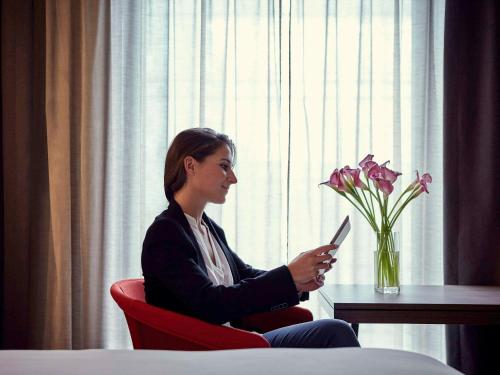 a woman sitting in a red chair holding a cell phone at Pullman Paris Roissy Cdg Airport in Roissy-en-France