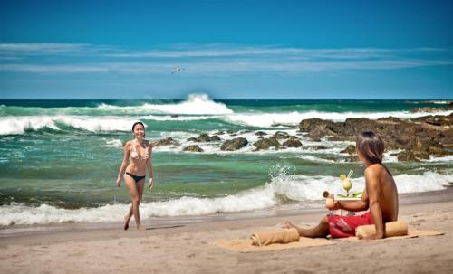a man and a woman sitting on a beach next to the ocean at Cala Luna Boutique Hotel & Villas in Tamarindo