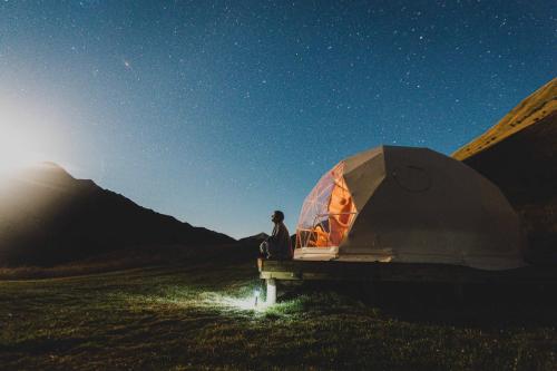 a man sitting next to a tent in a field at Glam Camping Queenstown in Queenstown