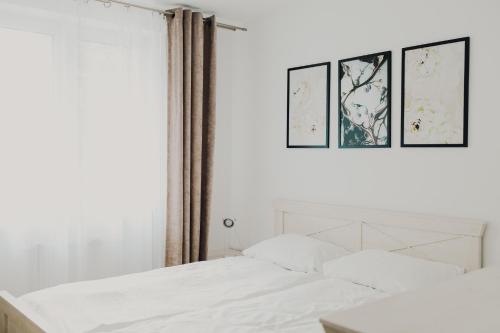 a bedroom with a white bed with three pictures on the wall at Apartamenty przy Dworku in Człuchów