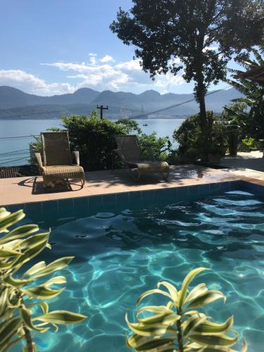 - une piscine avec 2 chaises et une vue sur l'eau dans l'établissement Casa com Piscina, Vista e Acesso ao Mar, à Angra dos Reis