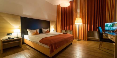 a bedroom with a bed and a desk and a television at Hotel Franziskushöhe Lohr in Lohr