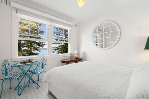 a white bedroom with a bed and two blue chairs at Manly Harbour in Sydney