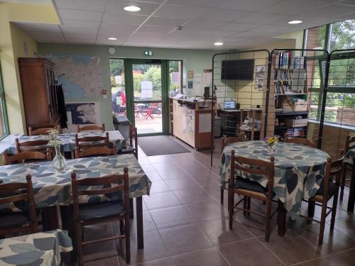 une salle à manger avec deux tables et des chaises ainsi qu'une cuisine dans l'établissement Ostal Scrignac - Gîte d'étape de la Gare, à Scrignac