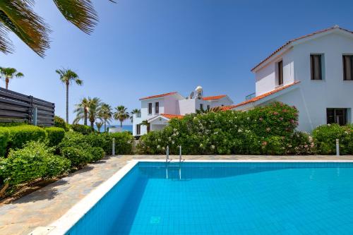 a villa with a swimming pool in front of a house at Platzia Beach Villas in Paphos City
