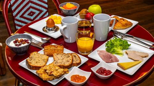 une table rouge avec un plateau de produits pour le petit-déjeuner dans l'établissement Novotel Suites Reims Centre, à Reims