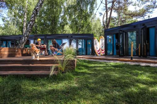 a couple and their dog sitting outside of a tiny house at Klimatyzowane Surf Domki - Maszoperia Sun4Hel - Letnia Baza SnowShow na Półwyspie Helskim in Jastarnia