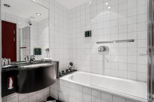 a white tiled bathroom with a tub and a sink at Home Hotel Bryggen in Bergen