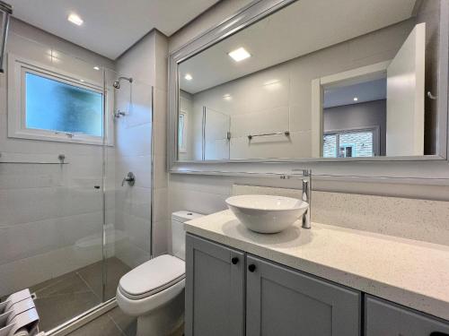 Un baño con lavabo, inodoro y espejo. en Casa de Pedra 2 Suítes e Piscina by Achei Gramado, en Gramado