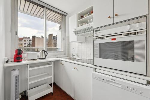 une cuisine avec des placards blancs et une grande fenêtre dans l'établissement Appartement calme et lumineux Place d'Italie by Weekome, à Paris