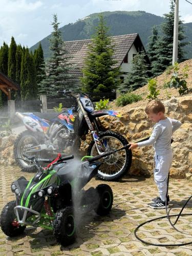 a young boy washing a dirt bike with a hose at Casa Mia Resort in Kupres