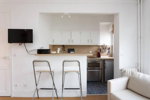 une cuisine avec des placards blancs et deux tabourets de bar dans l'établissement High standing Studio Paris 17, à Paris