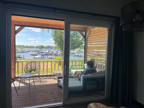 a woman sitting on a couch on a porch with a view of the water at Camping Kleine Belterwijde, Wiede Lodge met uitzicht over het water in Belt-Schutsloot