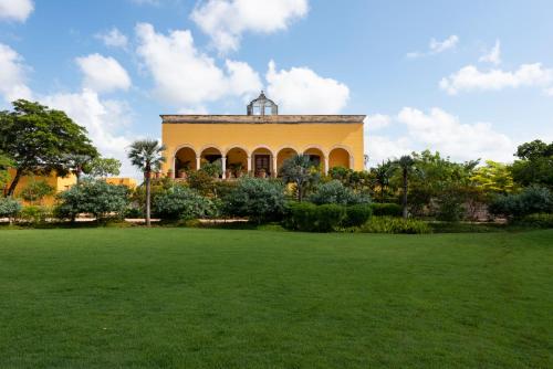a yellow building with a grass field in front of it at Hacienda San Antonio Hool in Mérida