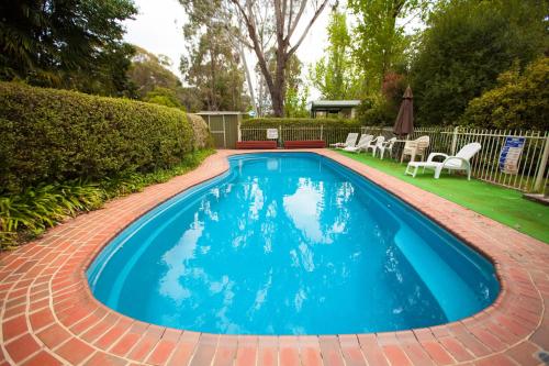a blue swimming pool with a brick pathway around it at Beechworth Holiday Park in Beechworth