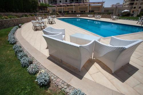 a swimming pool with white chairs and tables next to it at Rivoli Suites in Hurghada