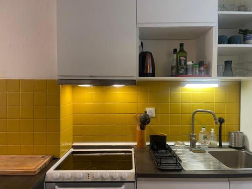 - une cuisine avec un évier et du carrelage jaune sur le mur dans l'établissement Cocon douillet avec jardin près de la mer, à Carqueiranne
