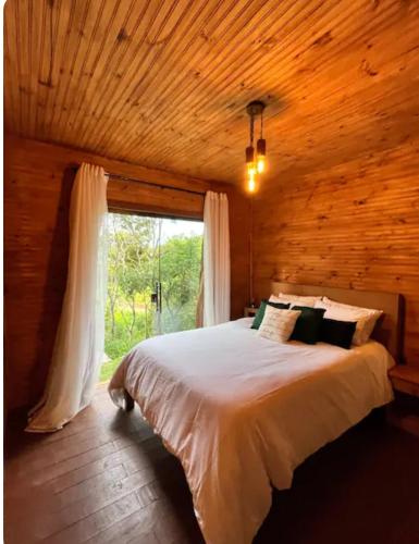 a bedroom with a large bed with a window at Cabana do Mato com ofurô, cesta para café da manhã e pet friendly in Gonçalves