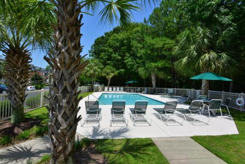 a pool with chairs and umbrellas next to a palm tree at 55F Pawleys After Dark condo by Peace Vacations in Pawleys Island
