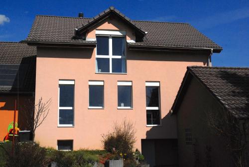 a pink house with white windows and a roof at Appartment Aux Lilas in Les Geneveys-sur-Coffrane
