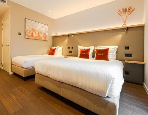 two beds with orange pillows in a hotel room at The CORNR Hotel in Nieuwpoort