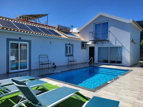 a swimming pool with chairs and a house at Vila Castro in Estreito da Calheta