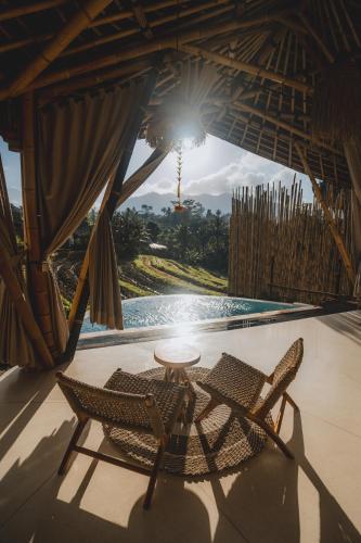 a patio with two chairs and a table and a pool at Nivriti Bali in Sidemen
