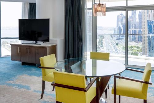 a dining room with a glass table and yellow chairs at Hilton Doha in Doha
