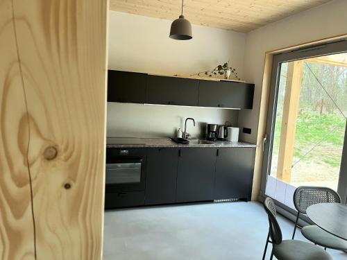 a kitchen with black cabinets and a table and a window at GRANIASTY - nowoczesny dom wakacyjny z basenem in Smażyno