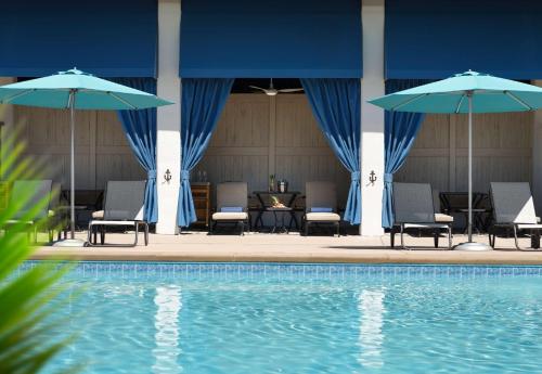 a pool with chairs and umbrellas next to a table and a table at The Ellie Beach Resort Myrtle Beach, Tapestry By Hilton in Myrtle Beach
