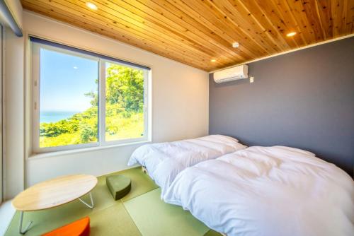 two beds in a room with a table and a window at 【南房テラス】180度パノラマオーシャンビュー絶景を楽しむリゾート別荘の家 in Kanaya