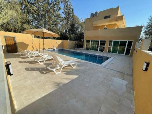 a house with a swimming pool with chairs and an umbrella at شاليهات ومسابح مزارع in Al Azraq ash Shamālī